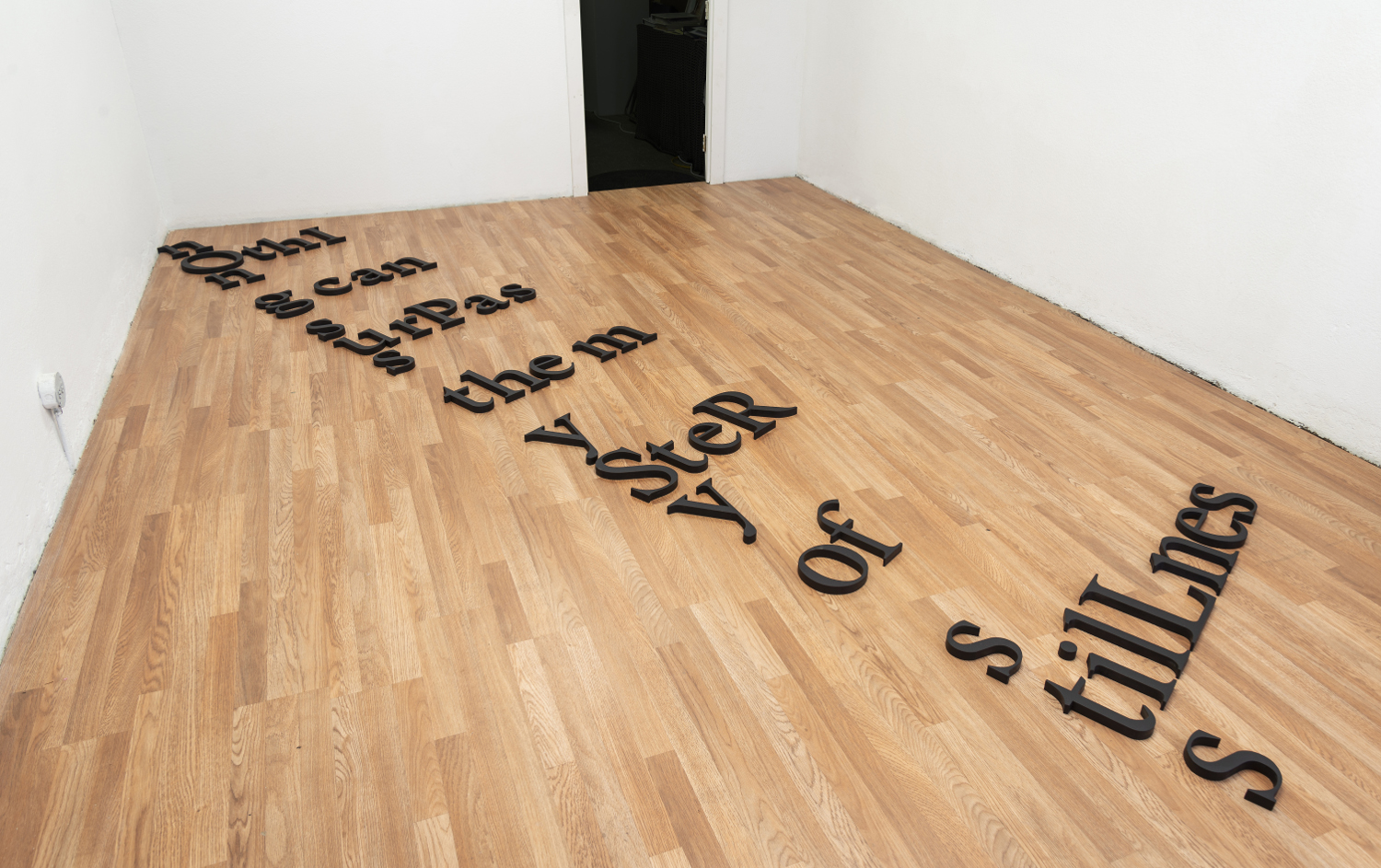 Exhibition installation: small black paintings hung in a line on a wall text on the floor