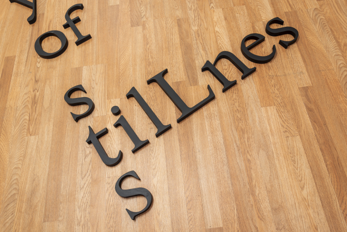 Exhibition installation: small black paintings hung in a line on a wall text on the floor