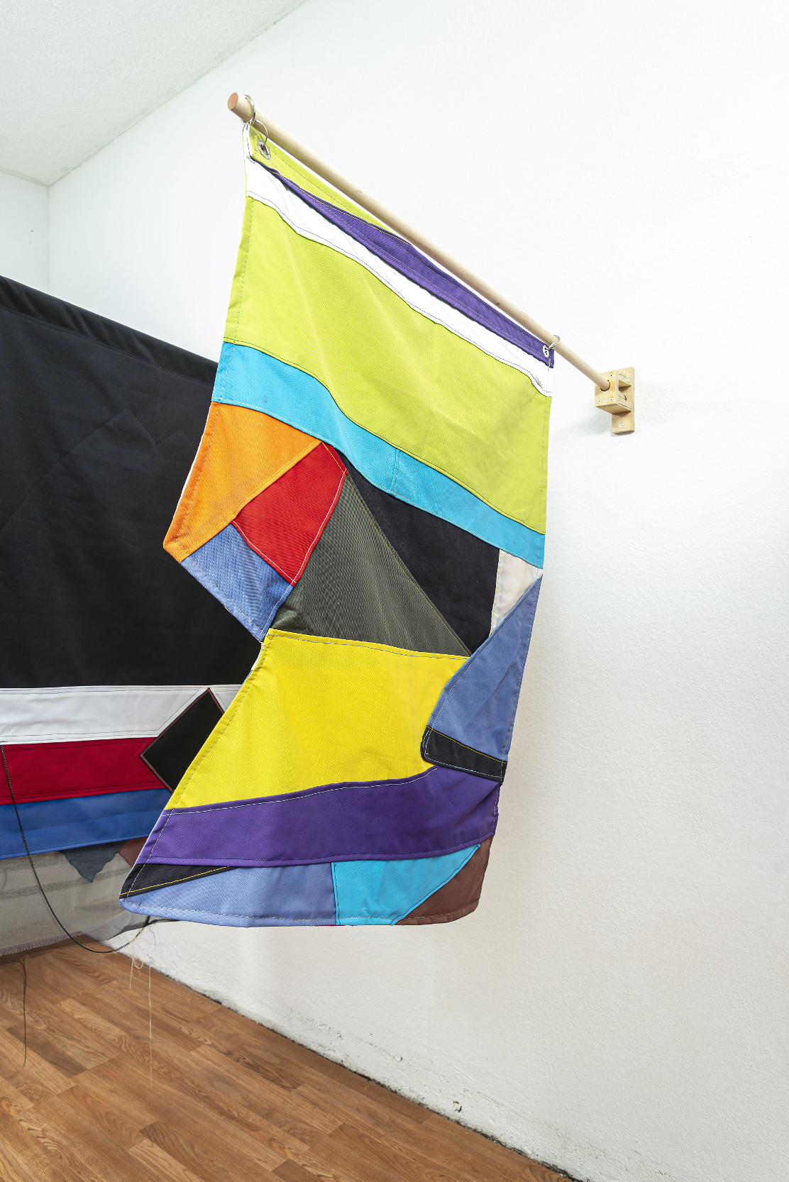 installation view: colorful flags hang in a clean well lit space with wooden floors and white walls