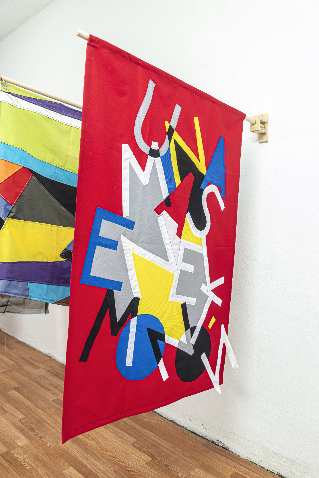 installation view: colorful flags hang in a clean well lit space with wooden floors and white walls