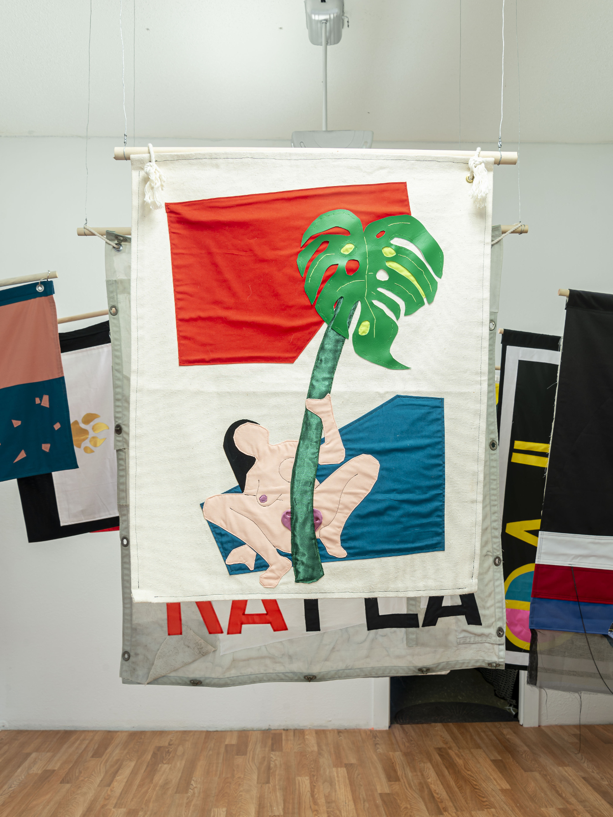 installation view: colorful flags hang in a clean well lit space with wooden floors and white walls