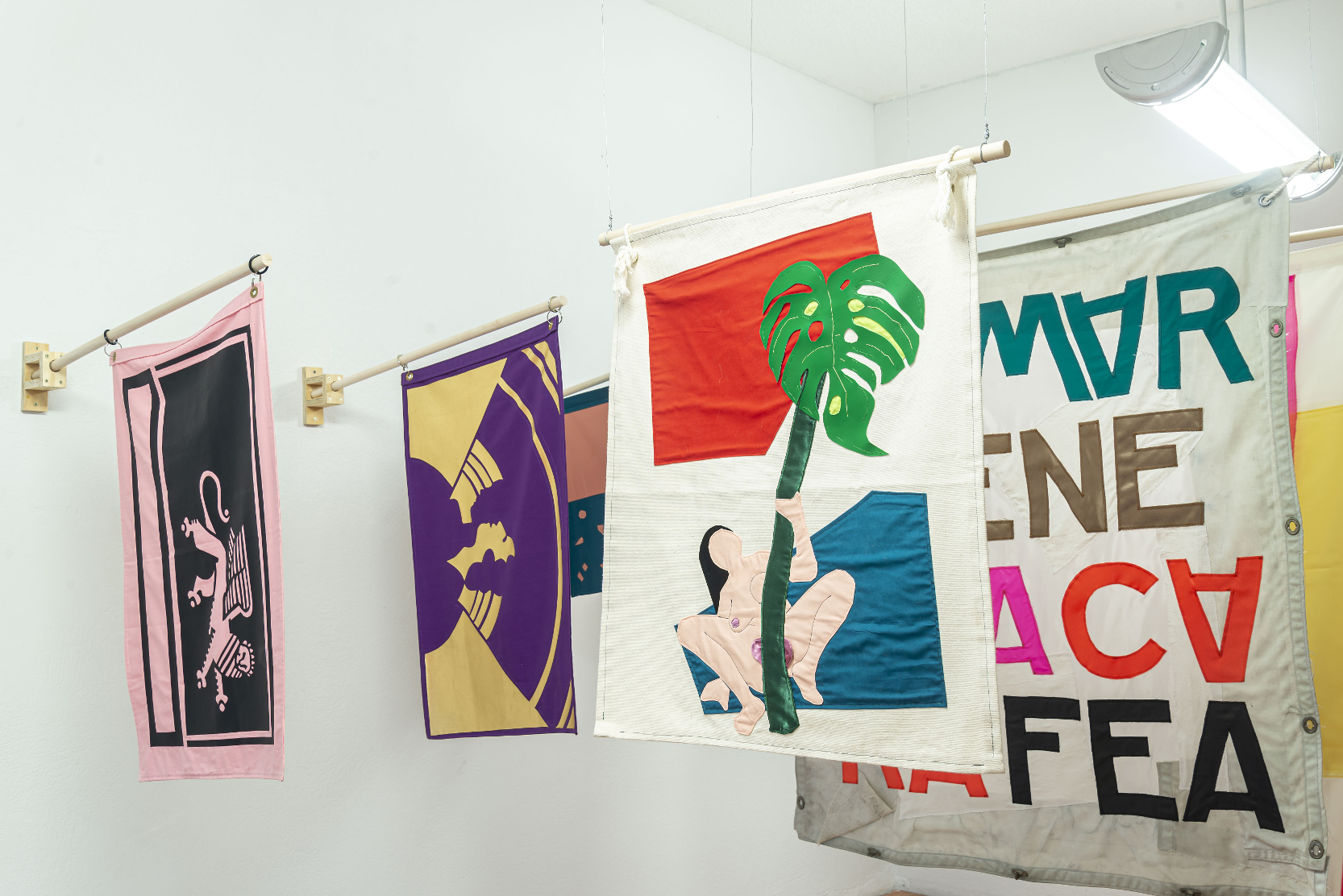 installation view: colorful flags hang in a clean well lit space with wooden floors and white walls